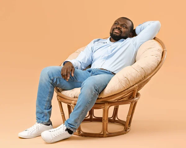 African-American man relaxing in armchair against color background — Stock Photo, Image