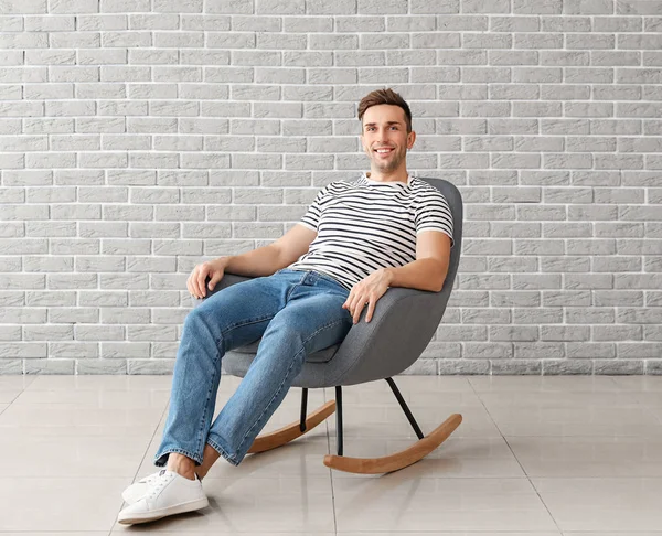 Handsome man sitting in armchair near brick wall