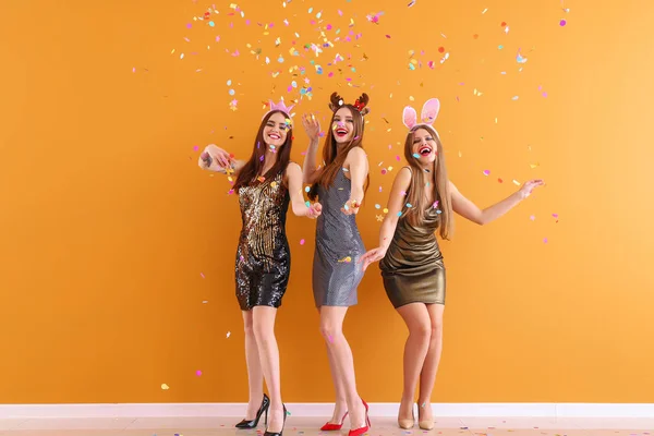 Mooie jonge vrouwen met party decor en confetti in de buurt van kleur muur — Stockfoto