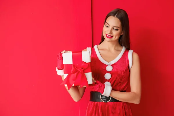Schöne junge Frau im Weihnachtsmannkostüm und mit Geschenk auf farbigem Hintergrund — Stockfoto