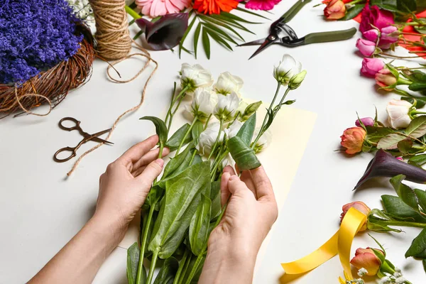 Female florist making beautiful bouquet on white background