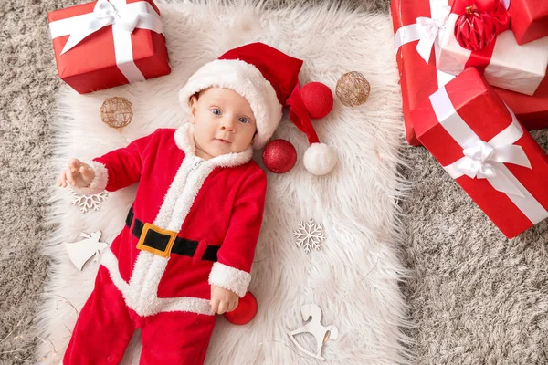 Niedliches kleines Baby im Weihnachtsmann-Kostüm und mit Weihnachtsgeschenkschachteln auf Plaid liegend, von oben gesehen — Stockfoto
