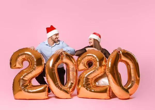 Gelukkig paar in Santa Claus hoeden en met luchtballonnen op kleur achtergrond — Stockfoto