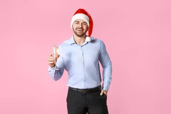 Beau jeune homme dans le chapeau du Père Noël et avec un verre de champagne sur fond de couleur — Photo