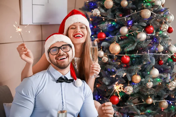 Happy young couple in Santa Claus hats and with champagne celebrating New Year at home — Stock Photo, Image