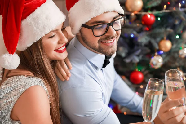 Feliz pareja joven en los sombreros de Santa Claus y con copas de champán en casa — Foto de Stock