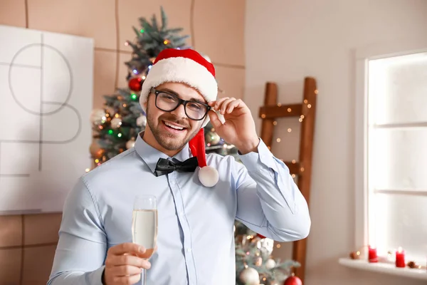 Joyeux jeune homme au chapeau de Père Noël et avec une coupe de champagne à la maison — Photo