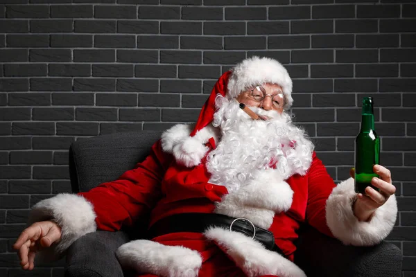 Engraçado bêbado Papai Noel sentado em poltrona contra o fundo de tijolo — Fotografia de Stock