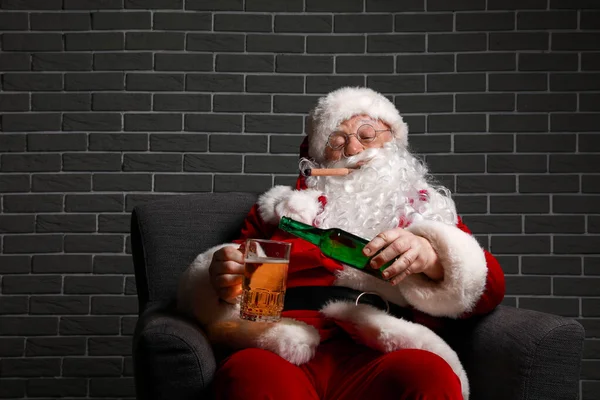 Funny drunk Santa Claus sitting in armchair against brick background — Stock Photo, Image