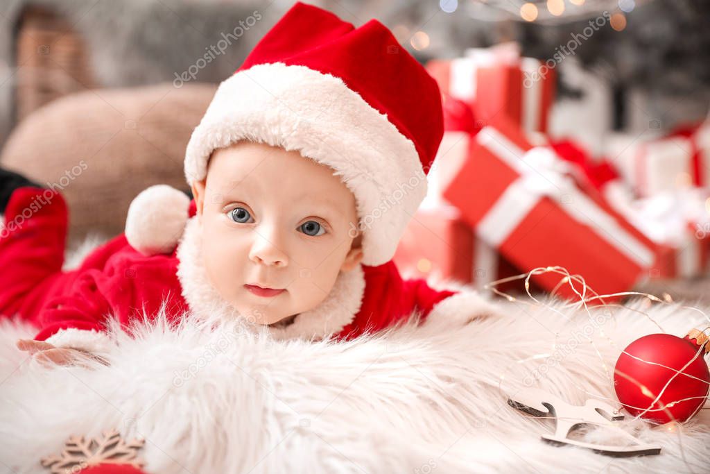 Cute little baby in Santa Claus costume lying on plaid at home