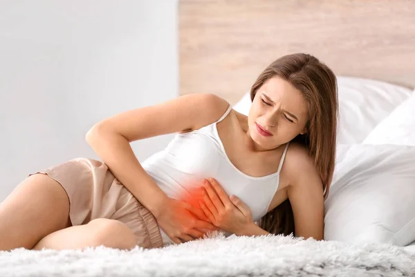 Young woman suffering from abdominal pain in bedroom — Stock Photo, Image