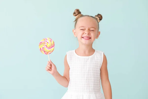 Cute little girl with sweet lollipop on color background — ストック写真