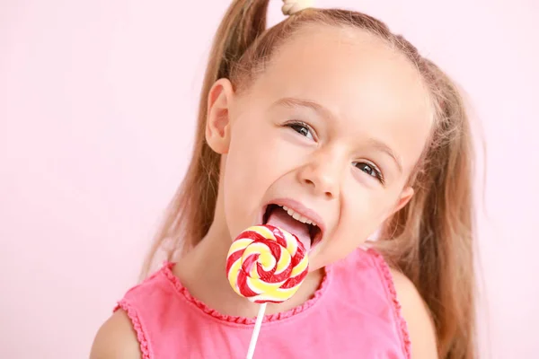 Cute little girl with sweet lollipop on color background — ストック写真