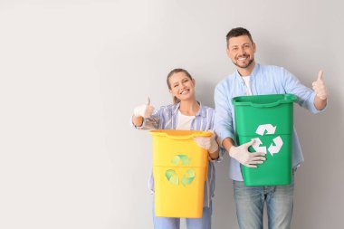 Çöp konteynırları olan bir çift beyaz arka planda baş parmağını gösteriyor. Geri dönüşüm kavramı