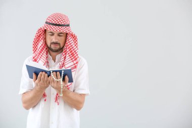 Kuran 'ı ve parlak arkaplanda boncukları olan Müslüman bir adam.