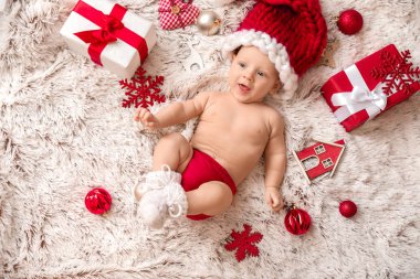 Noel Baba şapkalı şirin küçük bebek ve Noel hediyeleri ekose üzerinde yatıyor.