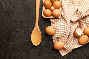 Koyu arkaplanda taze yumurta ve kaşık paketi var.