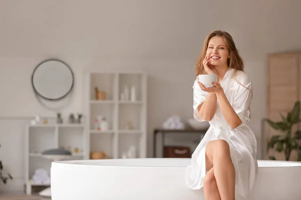 Schöne junge Frau trinkt Kaffee im Badezimmer — Stockfoto