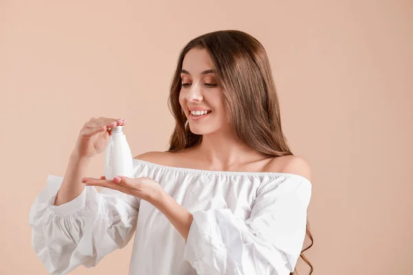 Beautiful young woman with bottle of cream on light background — Stock Photo, Image