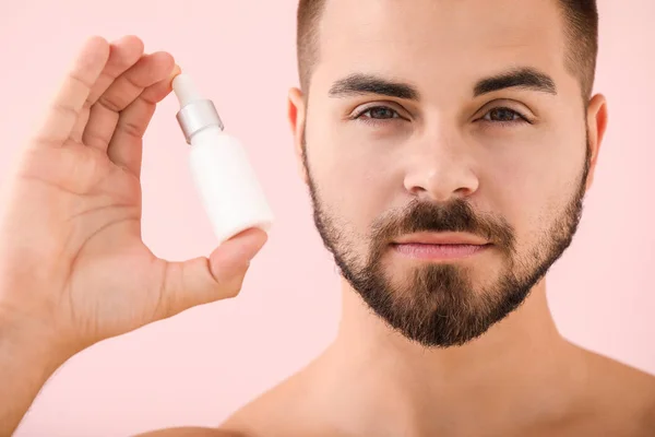 Schöner junger Mann mit kosmetischem Produkt auf farbigem Hintergrund — Stockfoto