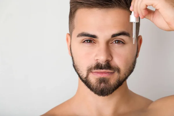 Knappe jongeman met cosmetisch product op lichte achtergrond — Stockfoto