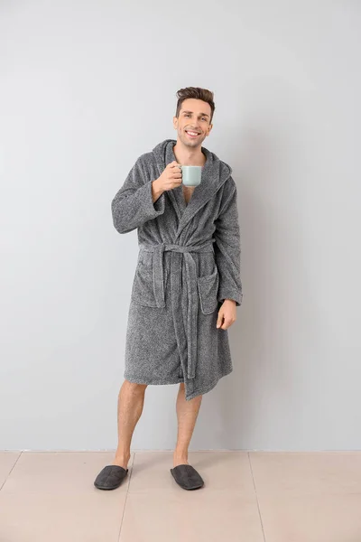 Handsome man in bathrobe and with cup of coffee near light wall — Stock Photo, Image