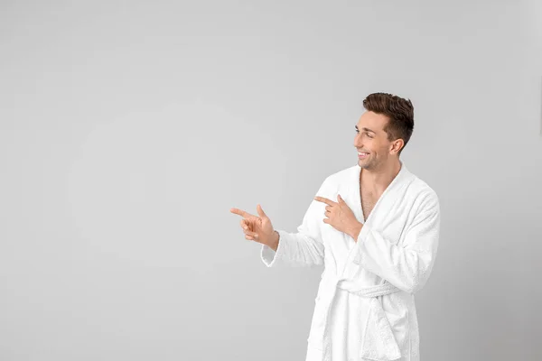 Hombre guapo en bata de baño apuntando a algo sobre fondo gris — Foto de Stock