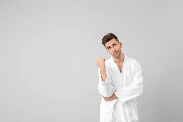 Hombre guapo en bata de baño apuntando a algo sobre fondo gris — Foto de Stock