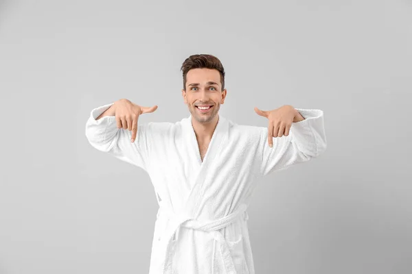 Hombre guapo en bata de baño apuntando a algo sobre fondo gris — Foto de Stock