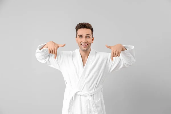 Handsome man in bathrobe pointing at something on grey background