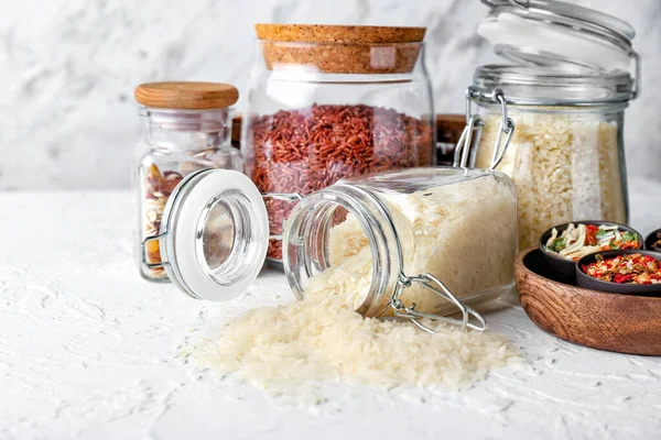 Jars with different raw rice, dry vegetables and spices on white table — Stock Photo, Image