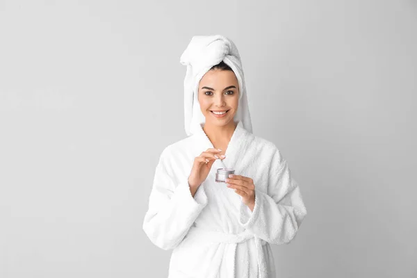 Beautiful young woman applying cream against grey background — ストック写真