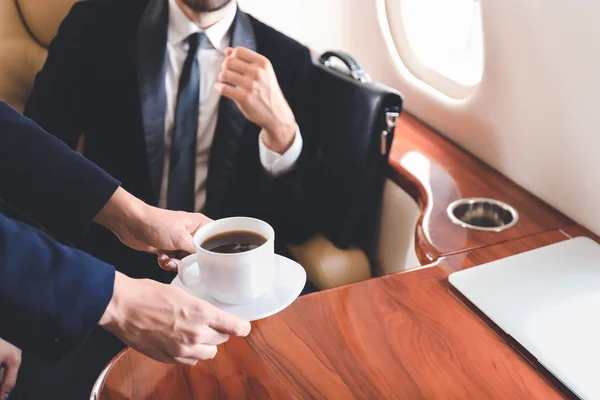 Air hostess bringing coffee for businessman on board the modern private airplane