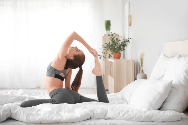 Beautiful young woman practicing yoga in bedroom — Stock Photo, Image