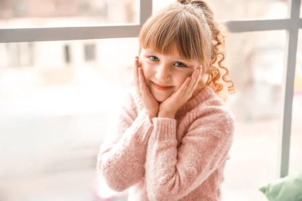 Cute little girl sitting on window sill at home — Stock Photo, Image