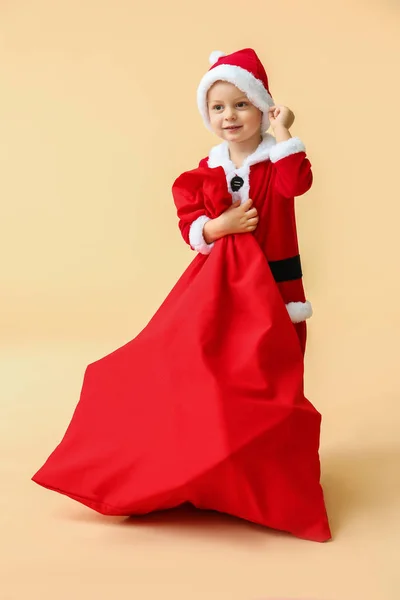 Mignon petit garçon en costume de Père Noël et avec sac plein de cadeaux de Noël sur fond de couleur — Photo