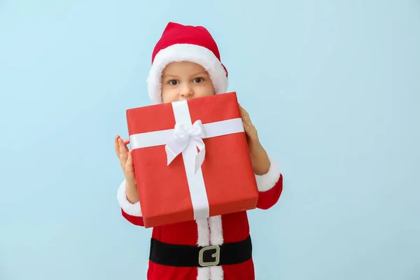 Niedlicher kleiner Junge im Weihnachtsmann-Kostüm und mit Weihnachtsgeschenk auf farbigem Hintergrund — Stockfoto