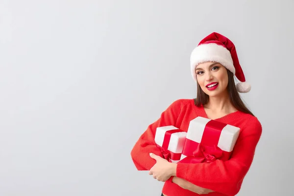 Noel Baba şapkalı güzel genç bir kadın ve ışık arka planında Noel hediyeleri. — Stok fotoğraf