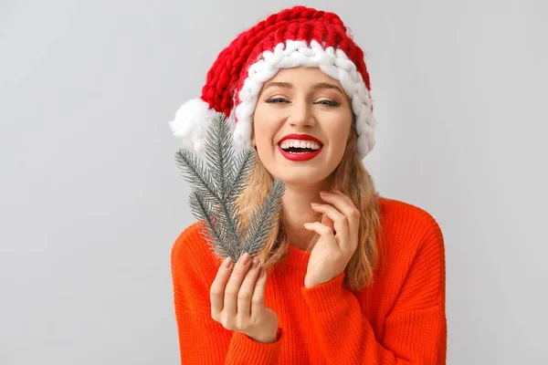 Bella giovane donna in cappello di Babbo Natale e con ramo di albero di Natale su sfondo chiaro — Foto Stock