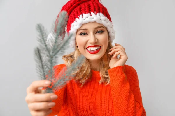 Mooie jonge vrouw in Santa hoed en met kerstboom tak op lichte achtergrond — Stockfoto