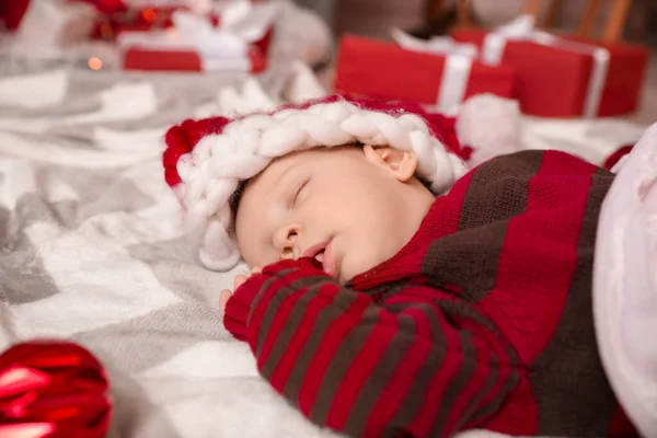 Bonito bebê em chapéu de Papai Noel dormindo em xadrez em casa — Fotografia de Stock