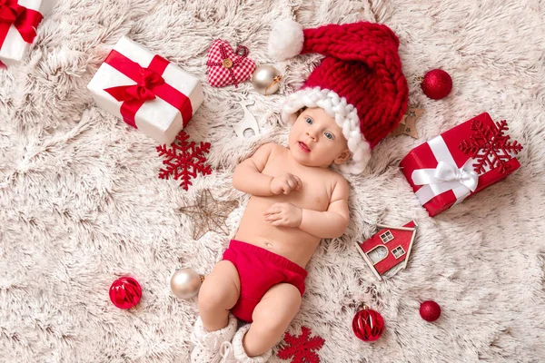 Cute little baby in Santa Claus hat and with Christmas gifts lying on plaid, top view — Stock Photo, Image