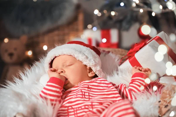 Cute little baby with Santa Claus hat and Christmas gift sleeping in basket at home — Stock Photo, Image