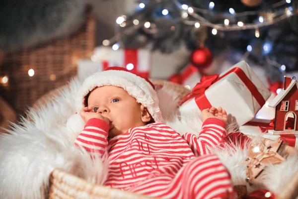 Bebê bonito com chapéu de Papai Noel e presente de Natal deitado em cesta em casa — Fotografia de Stock