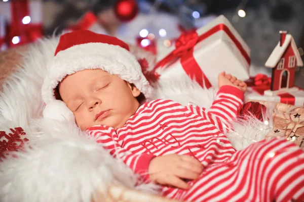 Bebê bonito com chapéu de Papai Noel e presente de Natal dormindo em cesta em casa — Fotografia de Stock