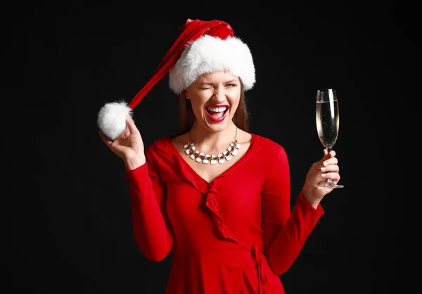Happy young woman in Santa Claus hat and with glass of champagne on dark background — Stock Photo, Image