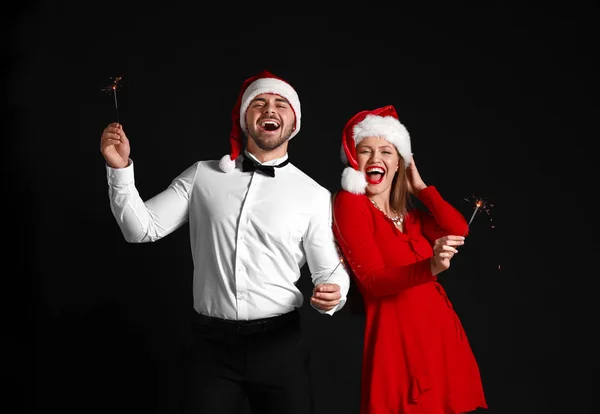 Ευτυχισμένο ζευγάρι σε καπέλα Αϊ-Βασίλη και με λαμπάδες Χριστουγέννων σε σκούρο φόντο — Φωτογραφία Αρχείου