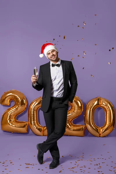 Bonito jovem no chapéu de Papai Noel e com copo de champanhe no fundo de cor — Fotografia de Stock