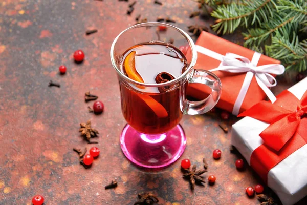 Стеклянная чашка вкусного глинтвейна, рождественские подарки и елки на столе — стоковое фото