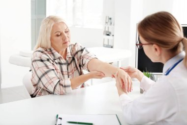 Klinikte eklem ağrısı olan olgun bir kadını muayene eden doktor.